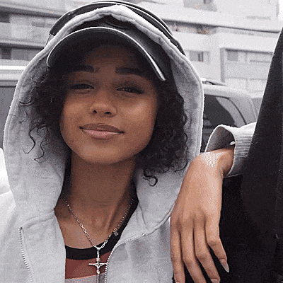 a woman with curly hair wearing a hat and a necklace with a cross on it