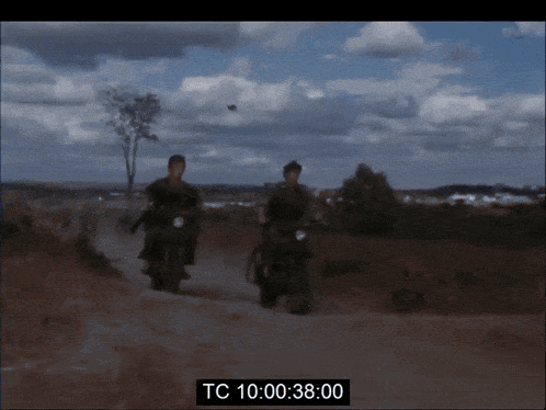 two men are riding motorcycles down a dirt road and the time reads tc 10 00 38 00