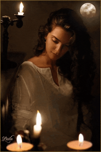 a woman in a white shirt is sitting in front of two lit candles with a full moon behind her
