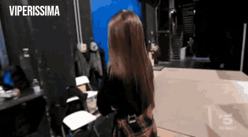 a woman in a plaid skirt is standing in front of a blue wall with the words viperissima written above her