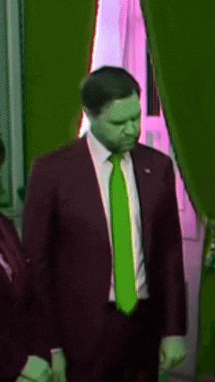 a man in a red suit and green tie stands in front of a window