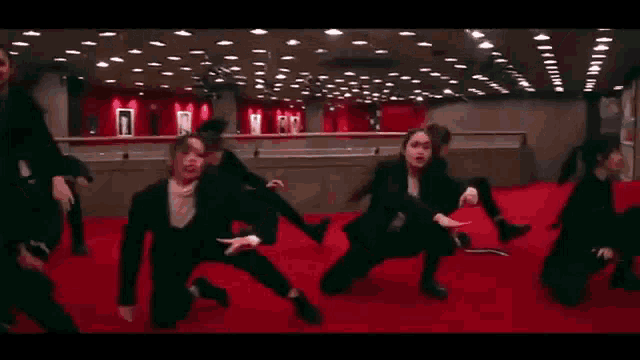 a group of women are dancing on a red carpet in a large room .