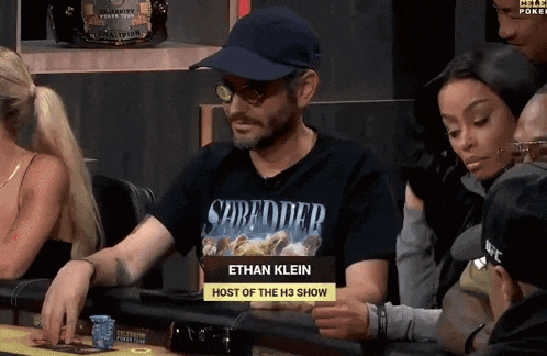 a man wearing a shirt that says " shredded " sits at a table with other people