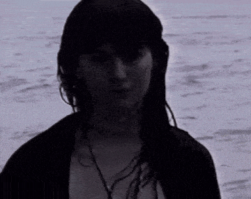 a woman with long dark hair is standing in front of the ocean
