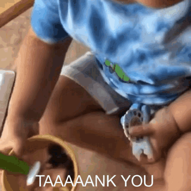 a baby in a blue shirt is playing with a toy and the words taaaaank you can be seen behind him