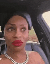 a woman is sitting in the back seat of a car with red lipstick and a necklace .