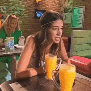 a woman sits at a table with two glasses of orange juice on it