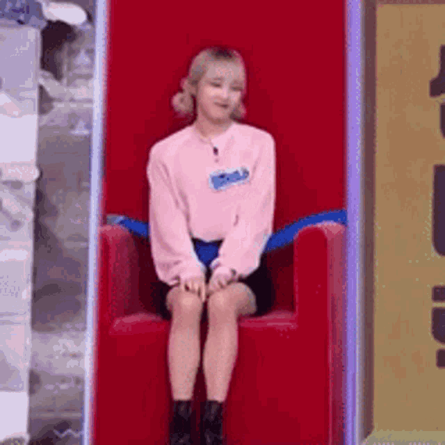 a woman in a pink sweater is sitting on a red chair .