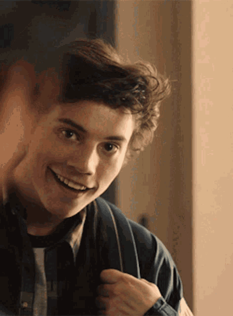 a young man with curly hair is smiling and holding a backpack