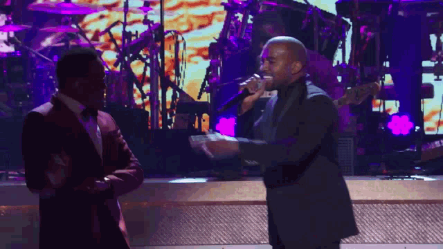 a man in a tuxedo singing into a microphone next to another man in a tuxedo
