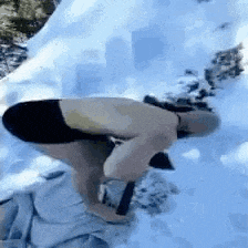 a person is squatting down in the snow while holding a hammer .
