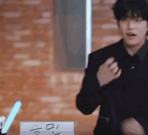 a man in a black suit is standing in front of a brick wall with a light stick .