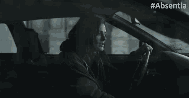 a woman is sitting in a car with #absentia on the bottom