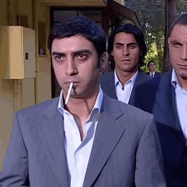 a man in a suit is smoking a cigarette in front of two other men