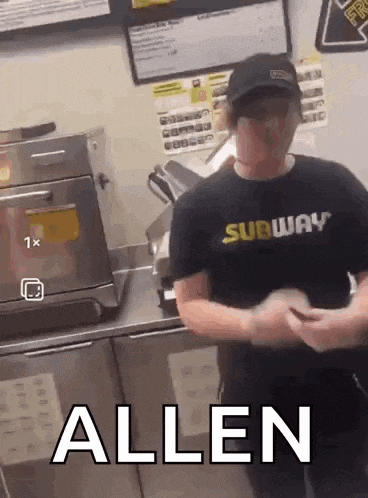 a man wearing a subway shirt is standing in front of a sandwich slicer .