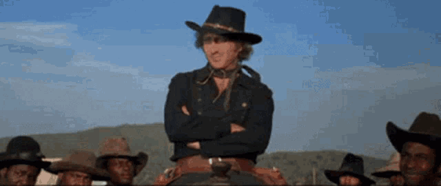 a man in a cowboy hat stands with his arms crossed in front of a group of cowboys