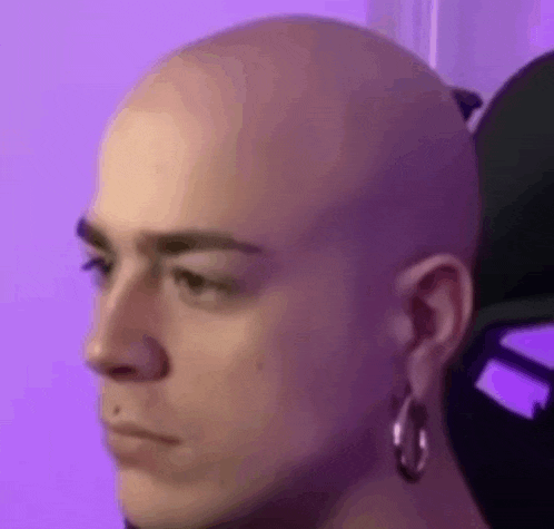a close up of a person 's face with a shaved head and earrings .