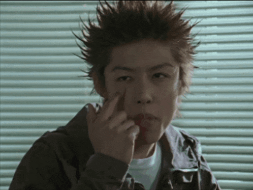 a man with spiky hair is covering his face with his finger
