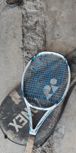a yonex tennis racket is laying on a dirty surface