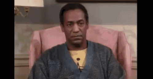 a man is sitting in a pink chair wearing a sweater and a yellow shirt .