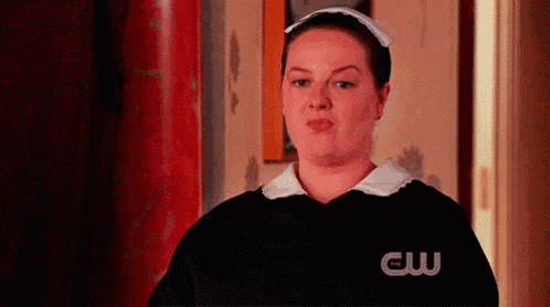 a woman in a maid costume is standing in a hallway making a funny face .