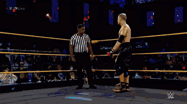 a man in a wrestling ring talking to a referee with # nxtlive written on the screen