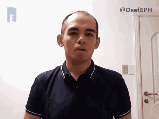 a man in a blue shirt is standing in front of a white wall with the hashtag @deafeph on it