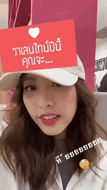 a woman wearing a white hat with a red sign that says " วาเลนไทน์ ปี นี้ "