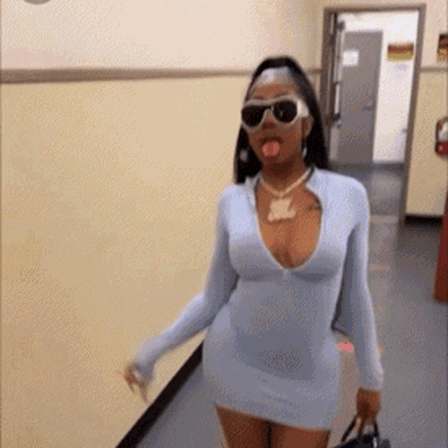a woman in a dress and sunglasses is walking down a hallway .
