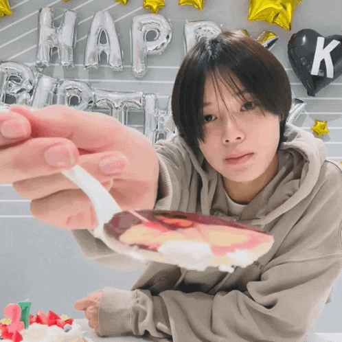 a person holding a spoon in front of a happy birthday balloon