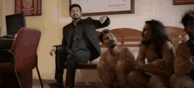 a man in a suit sits on a bench with a group of naked men sitting around him