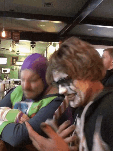 a man in a purple hat sits next to a man with face paint on