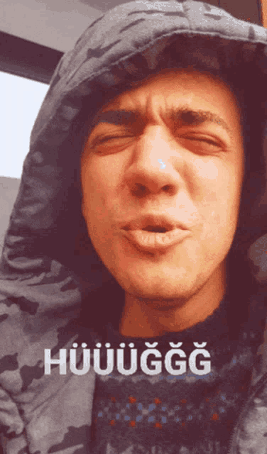 a man wearing a hooded jacket is making a funny face with the word huuuuggg written on his shirt