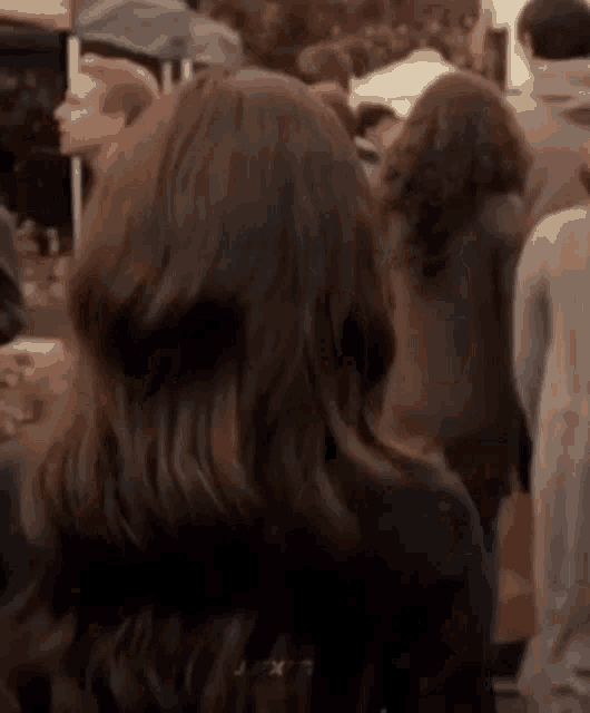 a woman with long brown hair is standing in a crowd of people and looking over her shoulder .