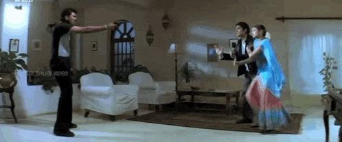 a man is pointing a gun at a woman in a living room while two other people are dancing .