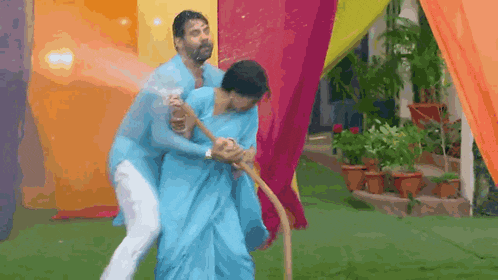 a man in a blue shirt is holding a woman in a blue saree while they play with a hose .