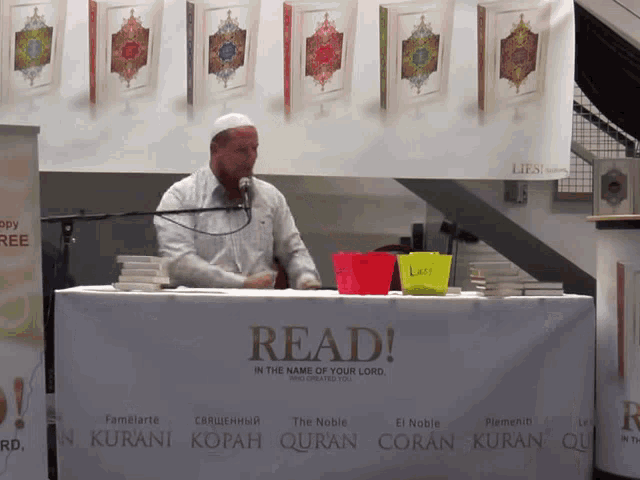 a man speaking into a microphone in front of a sign that says read
