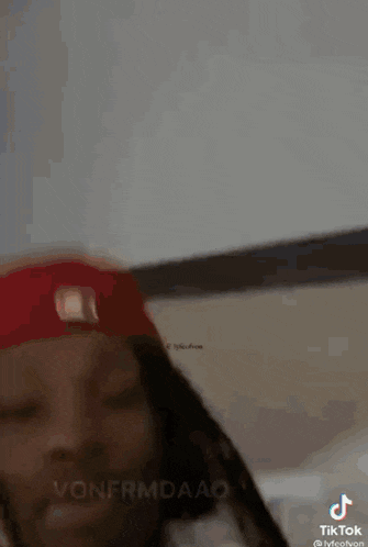 a man wearing a red hat and dreadlocks is standing in front of a white wall .