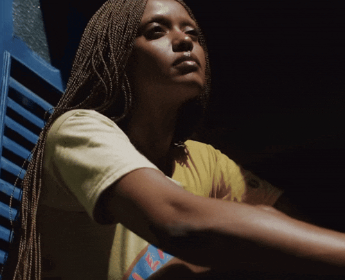 a woman with braids is wearing a yellow t-shirt with the letter e on it