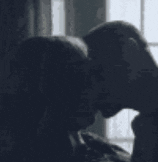 a man and a woman are kissing each other in front of a window .