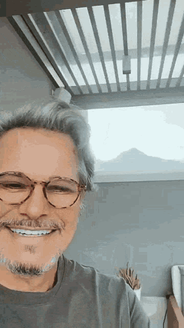 a man wearing glasses and a gray shirt smiles for the camera