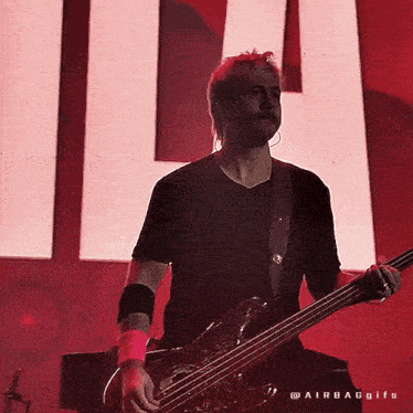 a man is playing a bass guitar in front of a large red sign .