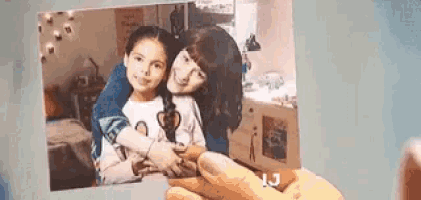 a person is holding a picture of two girls hugging each other in a bedroom .