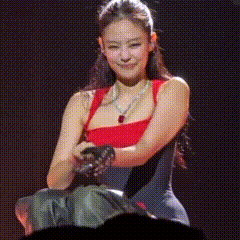 a woman in a red tank top is holding a microphone while sitting on a stage .