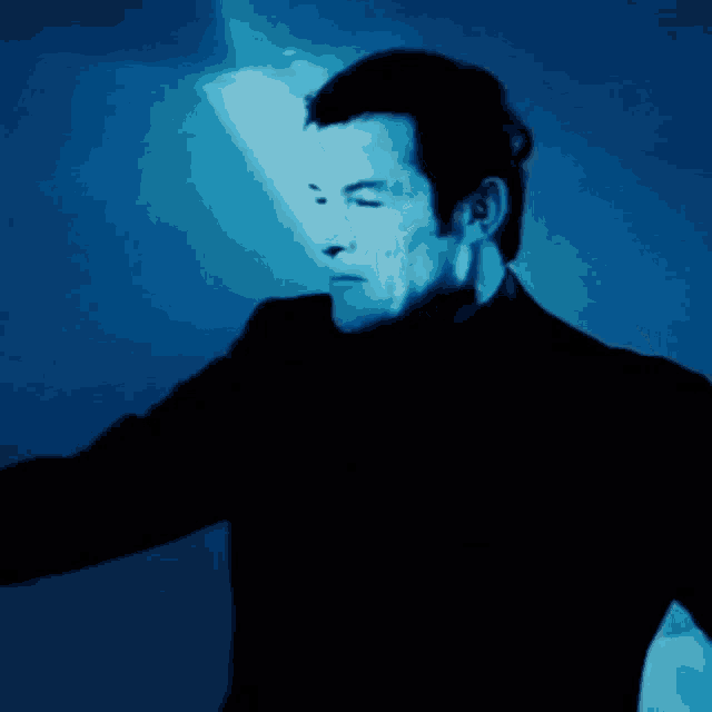 a man in a black suit stands in front of a blue wall