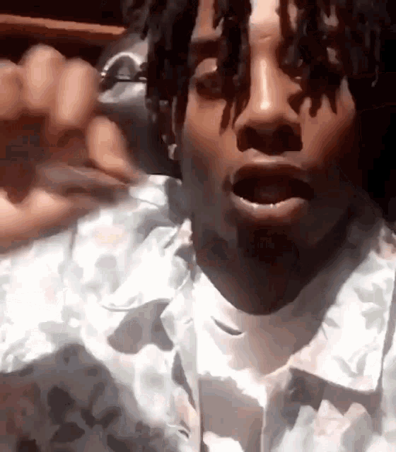 a man with dreadlocks is wearing a floral shirt and making a funny face