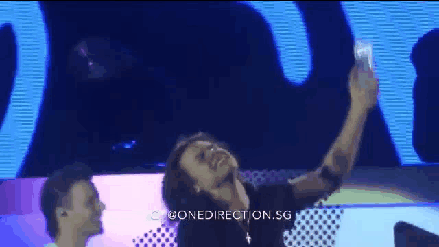 a man is taking a selfie on a stage while another man watches .