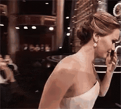 a woman in a white dress is talking on a cell phone while standing in front of a crowd .