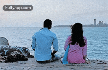 a man and a woman are sitting on the beach looking at the water .