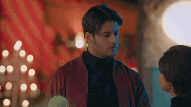 a man in a red jacket is looking at a woman in a black turtleneck .
